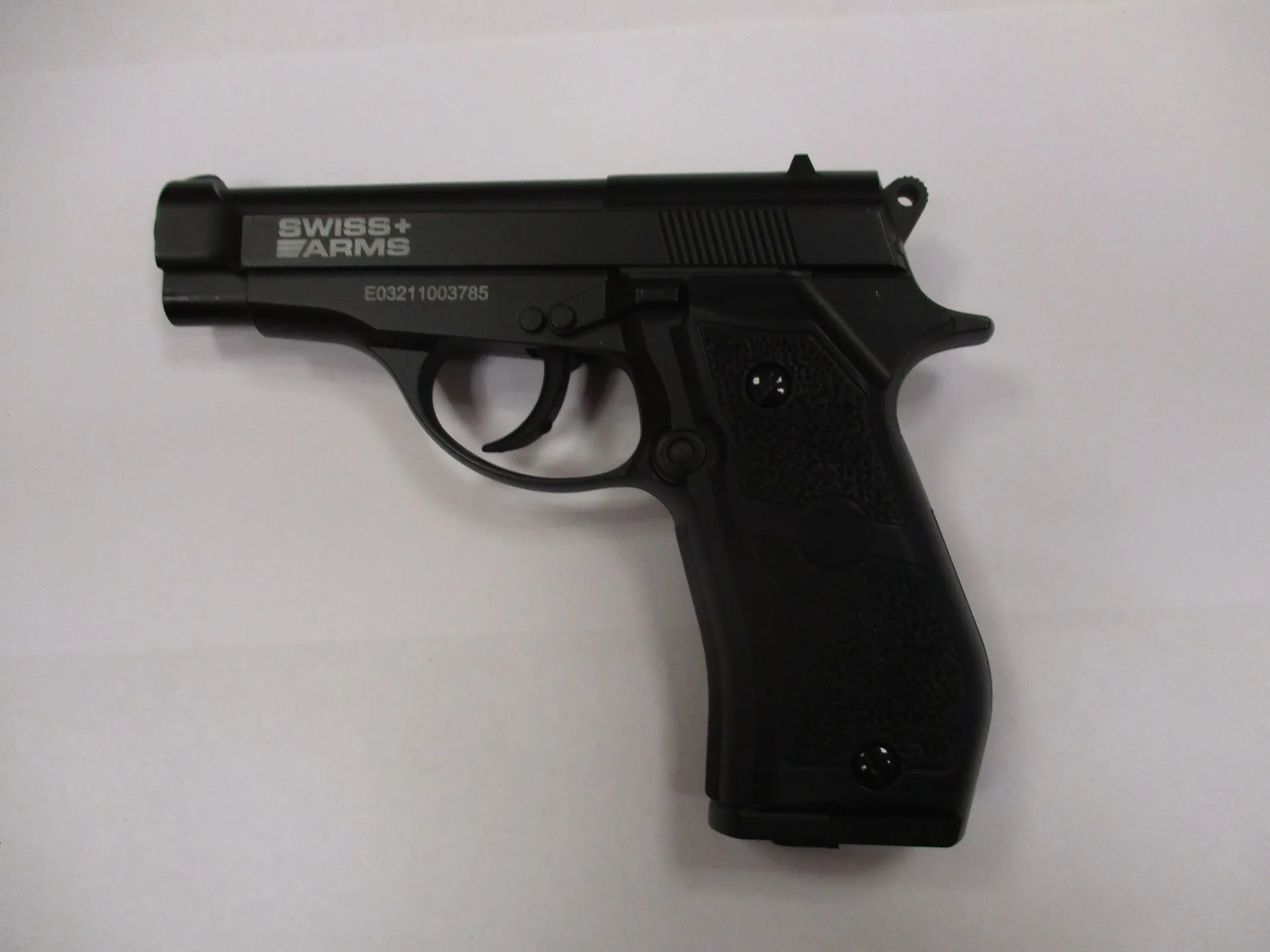 Czarny pistolet półautomatyczny na białym tle. Na zamku widnieje napis 'SWISS+ ARMS', a poniżej, na ramie, numer seryjny 'E03211003785'. Rękojeść posiada teksturowaną powierzchnię.