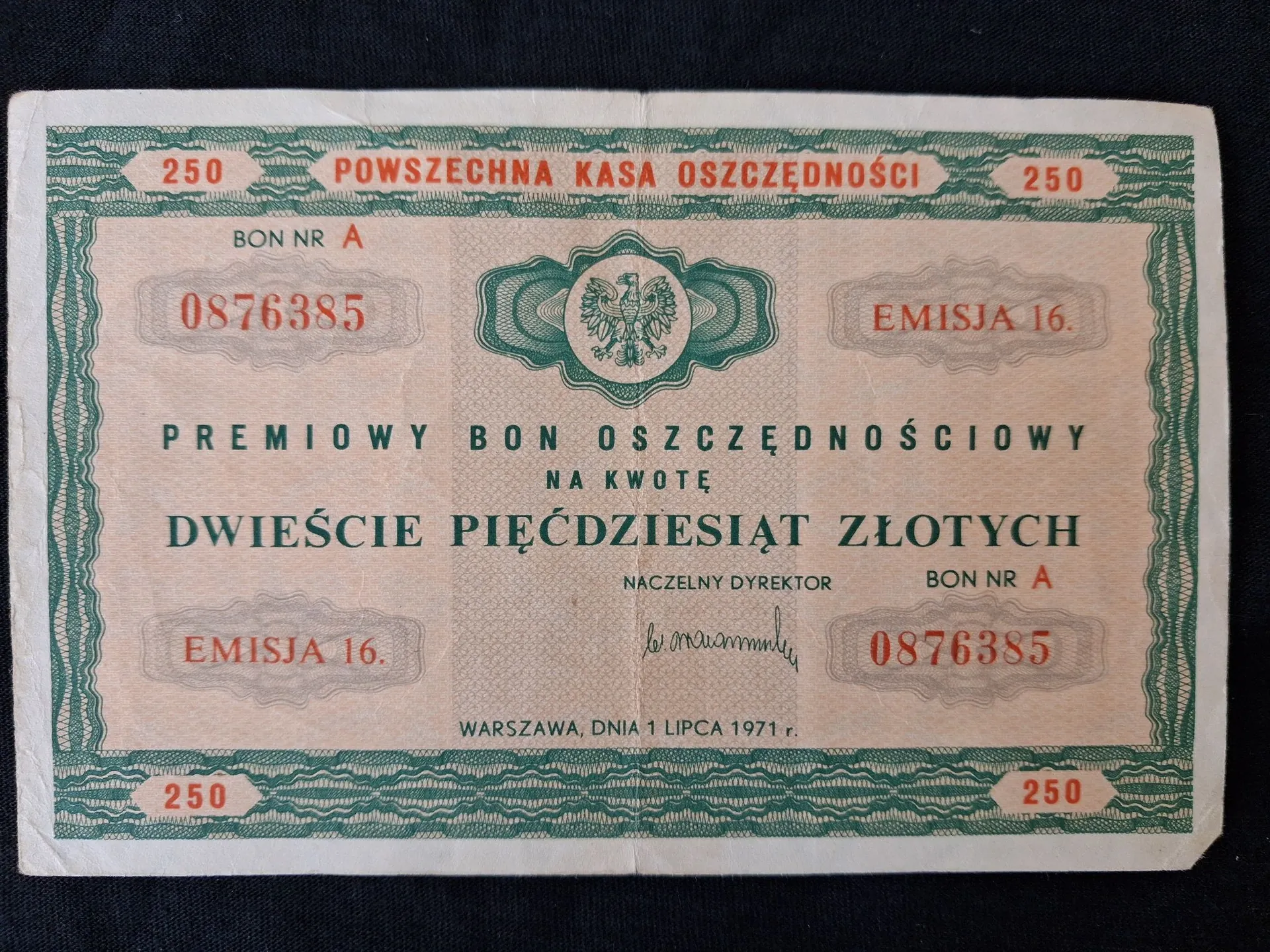 Stary, papierowy bon oszczędnościowy Powszechnej Kasy Oszczędności o nominale 250 złotych. Dokument ma beżowe tło z ozdobną, zieloną ramką i giloszami. W górnej części widnieje napis 'POWSZECHNA KASA OSZCZĘDNOŚCI' oraz liczba '250' po obu stronach. W centrum znajduje się godło Polski w okrągłym ornamentcie. Tekst główny brzmi: 'PREMIOWY BON OSZCZĘDNOŚCIOWY NA KWOTĘ DWIEŚCIE PIĘĆDZIESIĄT ZŁOTYCH'. Na dokumencie widnieją numery seryjne '0876385', oznaczenie 'EMISJA 16.', podpis Naczelnego Dyrektora oraz data 'WARSZAWA, DNIA 1 LIPCA 1971 r.'