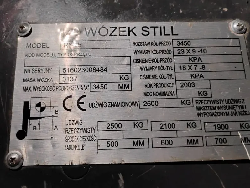 Srebrna tabliczka znamionowa wózka widłowego marki STILL. Zawiera ona następujące dane: Model: R6 25, Numer seryjny: 516023008484, Masa wózka: 3137 KG, Maksymalna wysokość podnoszenia 'A': 3450 MM, Rozstaw kół przednich: 3450, Wymiary kół przednich: 23 X 9 - 10, Wymiary kół tylnych: 18 X 7 - 8, Rok produkcji: 2003, Udźwig znamionowy: 2500 KG. W dolnej części znajduje się tabela z udźwigiem rzeczywistym w zależności od środka ciężkości ładunku 'B': dla 500 MM jest to 2500 KG, dla 600 MM jest to 2100 KG, a dla 700 MM jest to 1900 KG. Po lewej stronie widoczny jest schemat techniczny oraz znak CE.