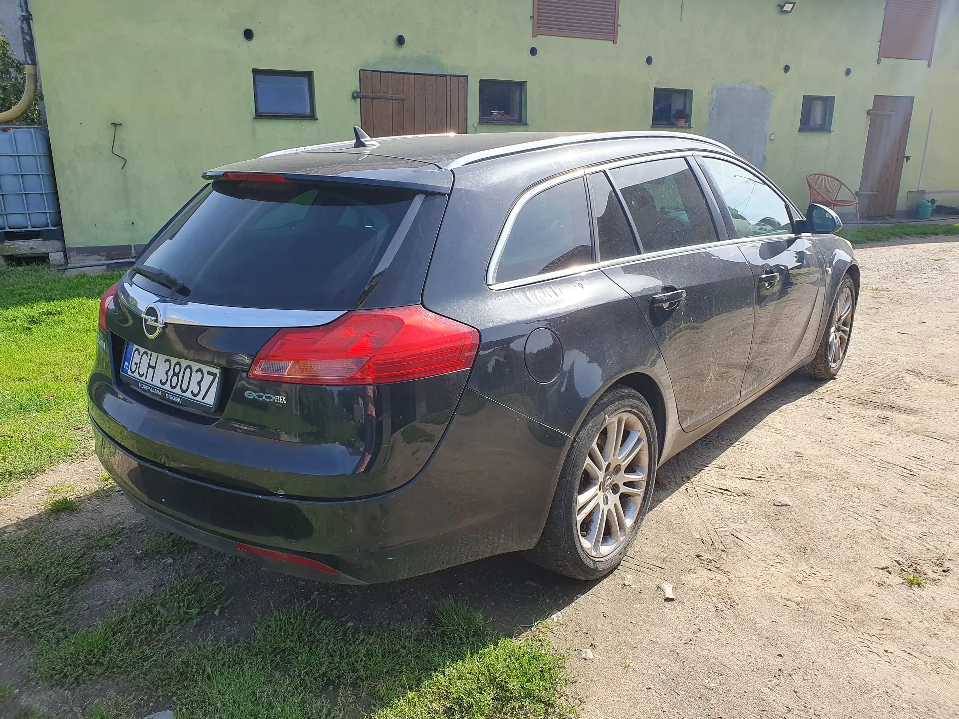 Czarny samochód osobowy typu kombi zaparkowany na piaszczystym podjeździe przed jasnozielonym budynkiem. Widoczna jest tylna i boczna część pojazdu. Samochód ma tablicę rejestracyjną o numerze GCH 38037 oraz oznaczenie ecoFLEX na klapie bagażnika.