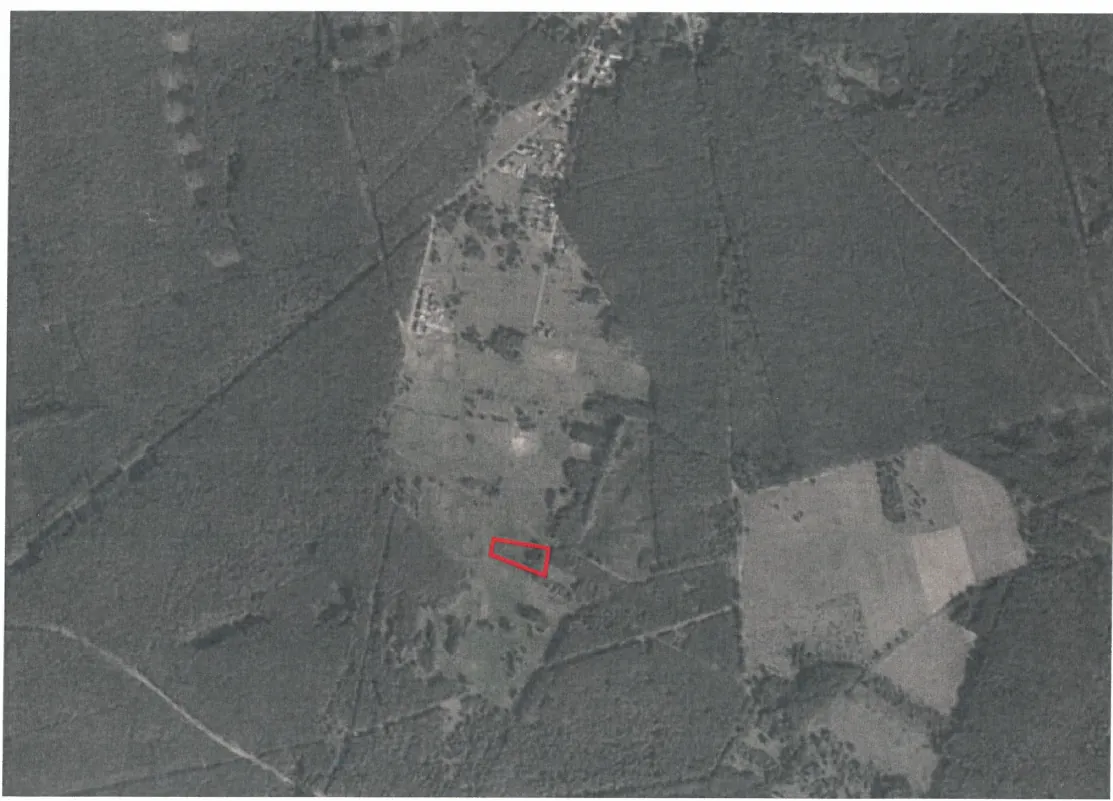 Czarno-białe zdjęcie satelitarne przedstawiające obszar wiejski z polami, drogami i rozproszonymi budynkami. W centralnej części obrazu znajduje się czerwony prostokąt zaznaczający konkretny fragment terenu. Widoczne są również linie dróg przecinających obszar oraz różne tekstury pól i lasów.