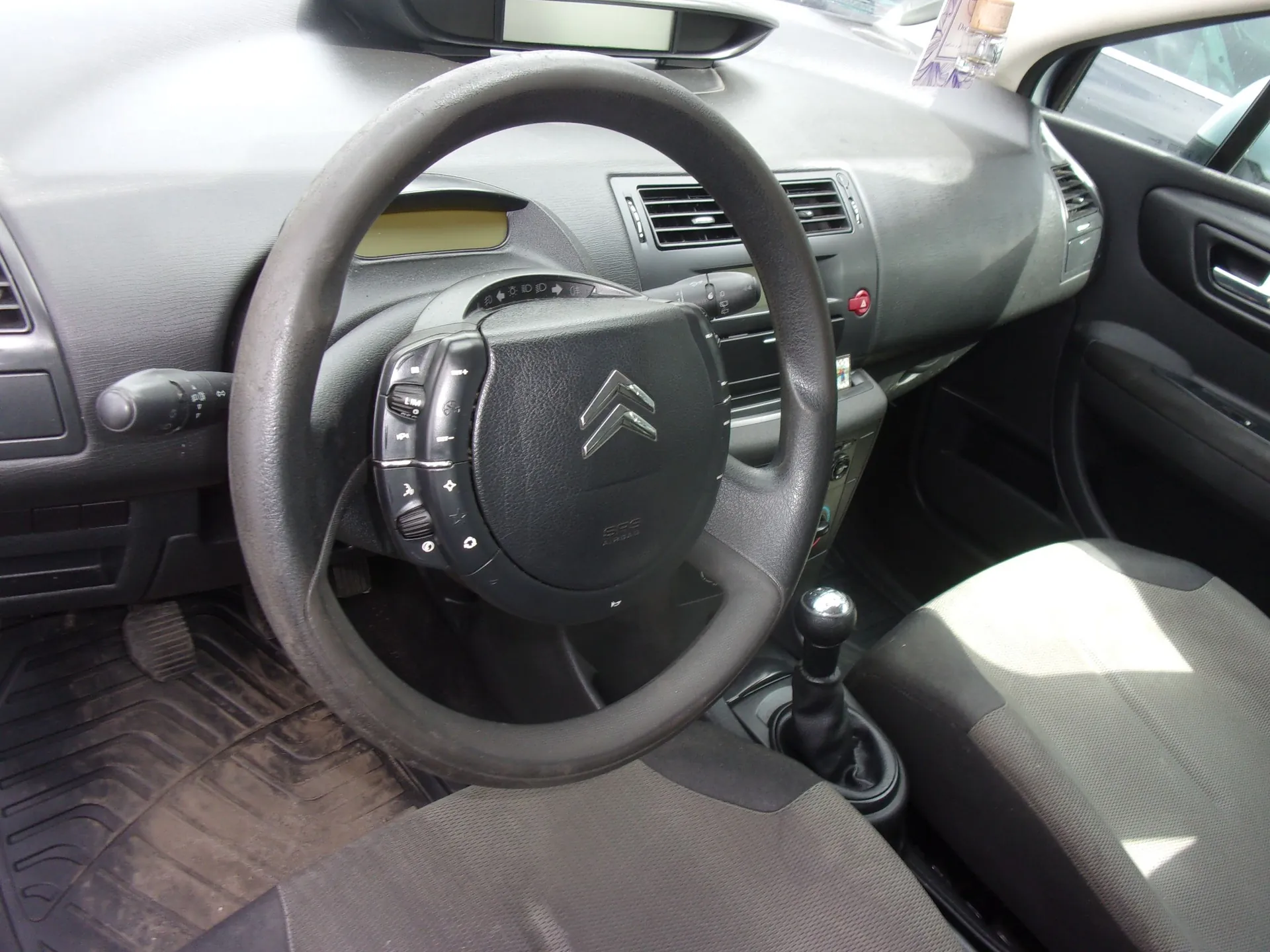 Wnętrze samochodu marki Citroën widziane z perspektywy kierowcy. Widoczna jest czarna, skórzana kierownica z logo marki na środku, deska rozdzielcza, lewarka kierunkowskazów, drążek zmiany biegów oraz dwa przednie fotele z ciemnoszarą tapicerką.